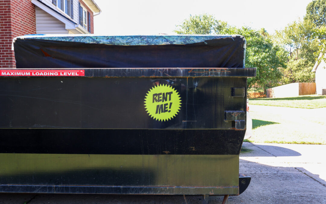 A rented dumpster in a residential driveway with a "Rent Me" sticker on it.